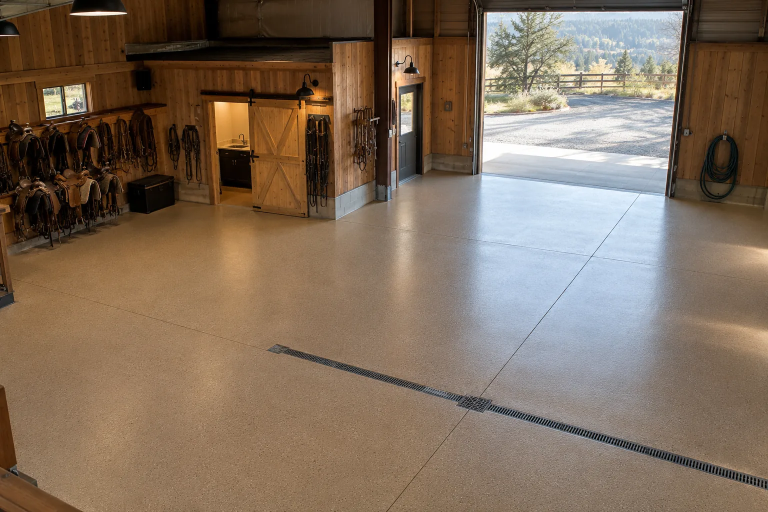 Tack room and shop floor in tan epoxy with a trench drain, saddles on the wall and a hose beside the open door