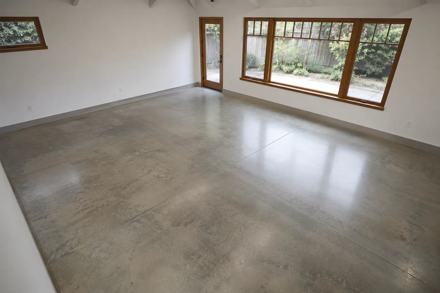 Empty studio room with a ground and polished concrete floor showing soft sheen and subtle aggregate beside a wood-framed window