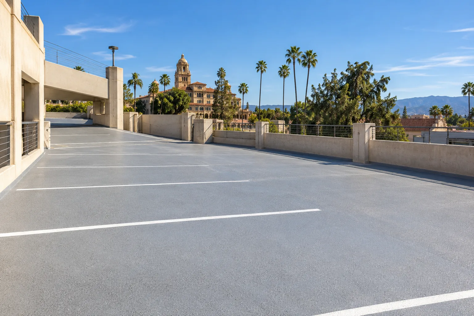 Upper parking deck coated in gray traffic membrane with white stall lines, a rail and a historic tower with palm trees beyond