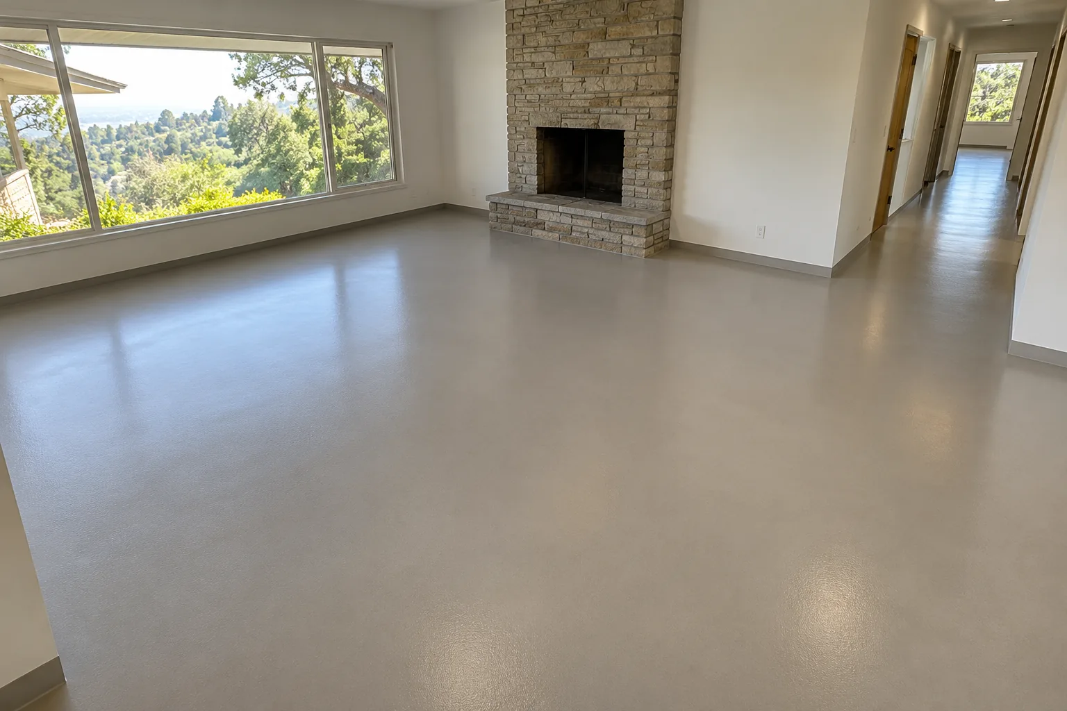 Seamless warm gray satin epoxy floor in an empty family room with a stone fireplace and a hallway beyond